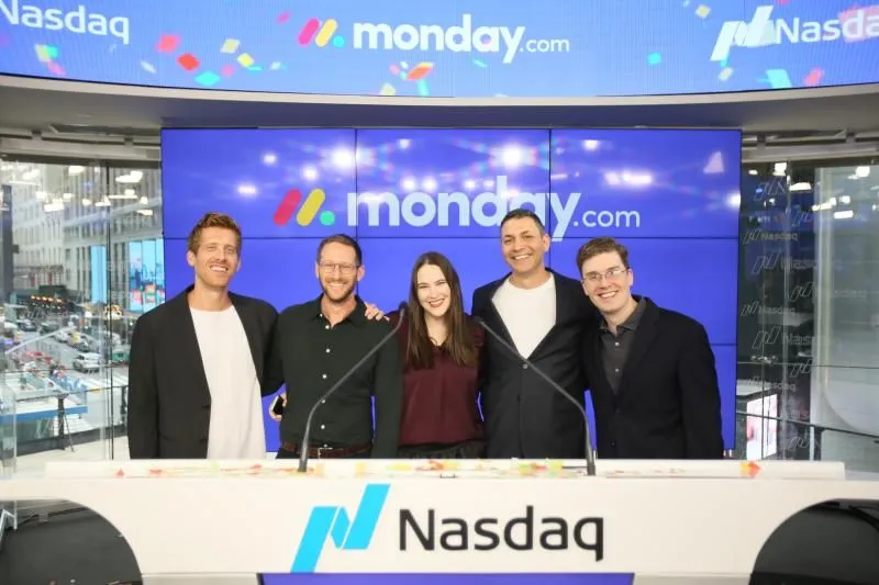 Matt Burns stands with four monday.com teammates behind the Nasdaq podium on IPO day, with confetti falling across the screens and the monday.com logo overhead.