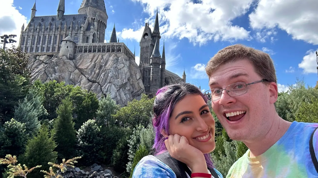 Matt and Nicole Burns grin into a selfie in front of the Hogwarts castle at the Wizarding World of Harry Potter.